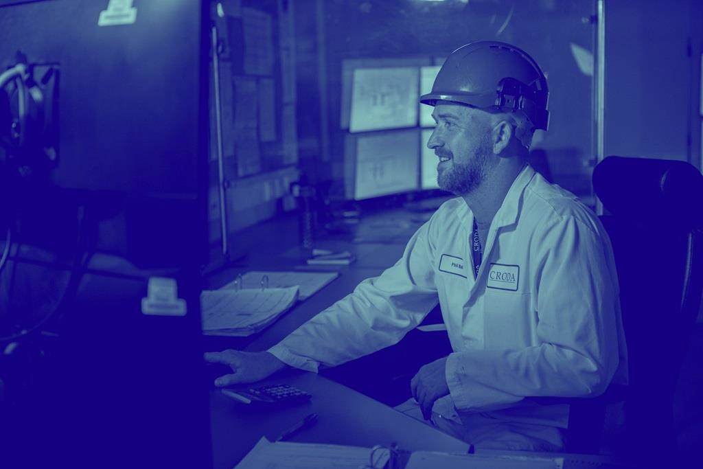 blue washed image of male at computer wearing hard hat