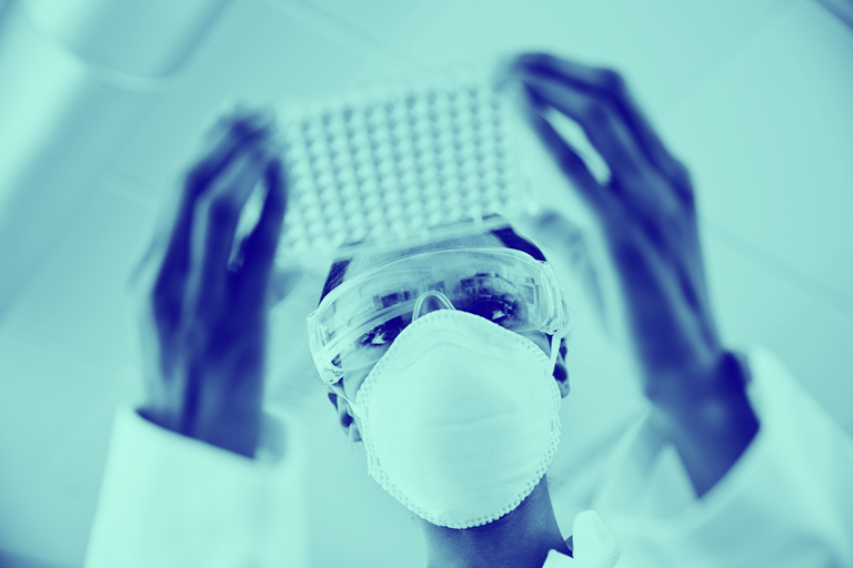 Blue washed image of female in lab wearing mask looking into tray