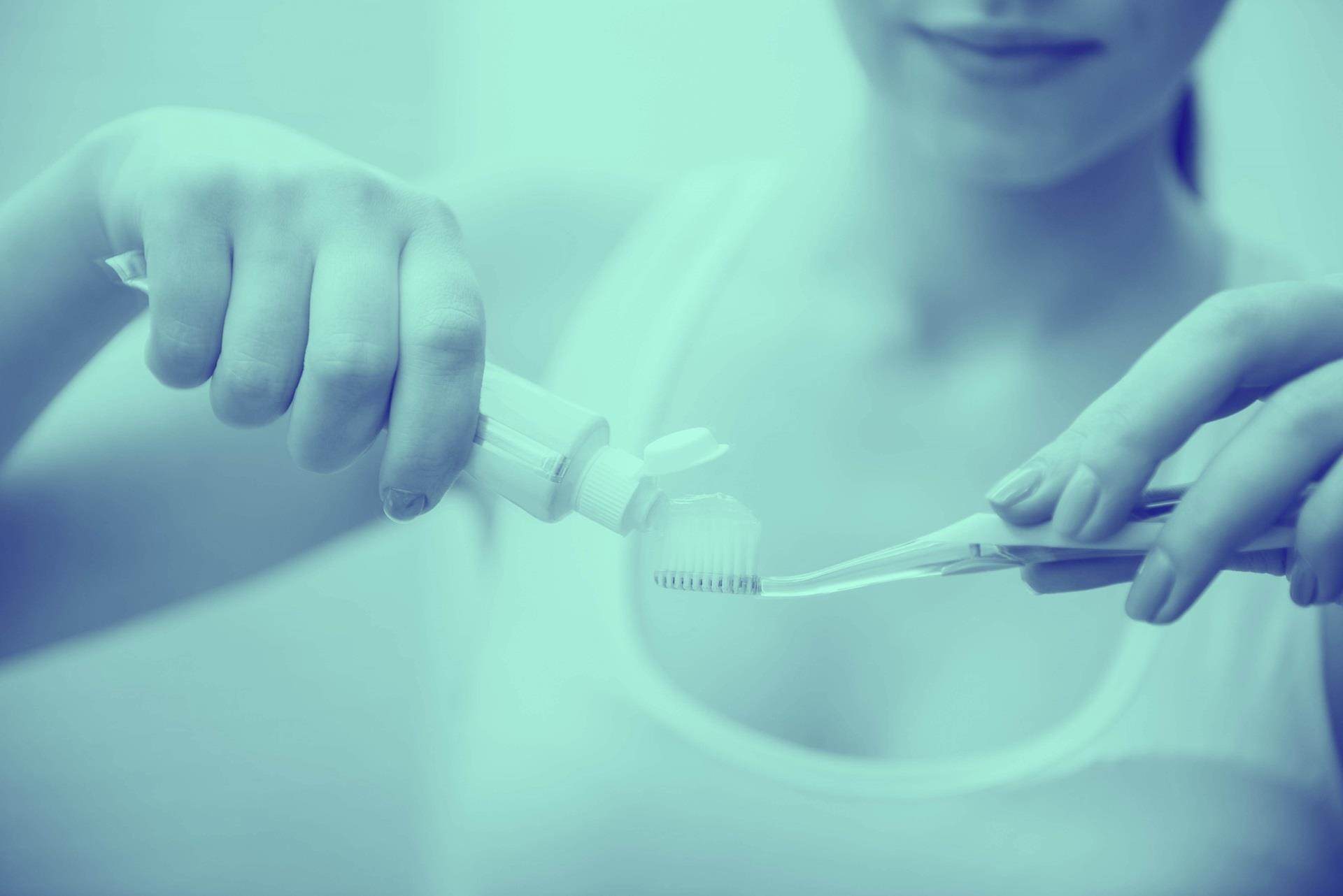 Close-up of woman is holding a toothbrush and placing toothpaste on it.