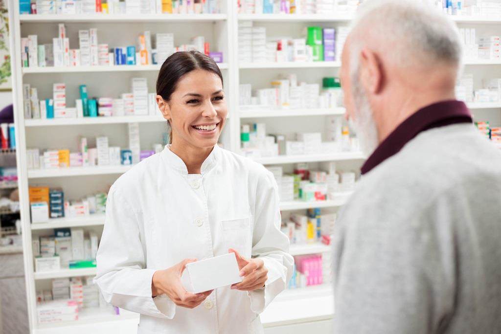Happy female pharmacist giving medications to senior male customer