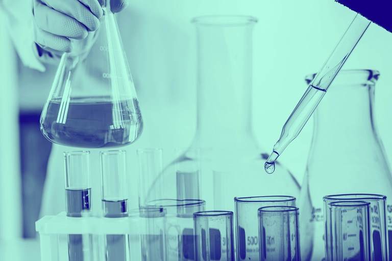 化学実験室の背景に実験用ガラス器具が入ったフラスコを保持している科学者